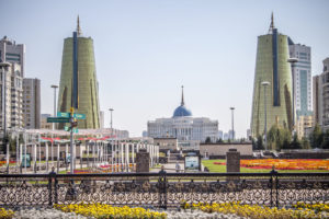 Vy över presidentpalatset i Kazakstan med en gul- och rödblommig parkmiljö i förgrunden och stora torn på sidorna.