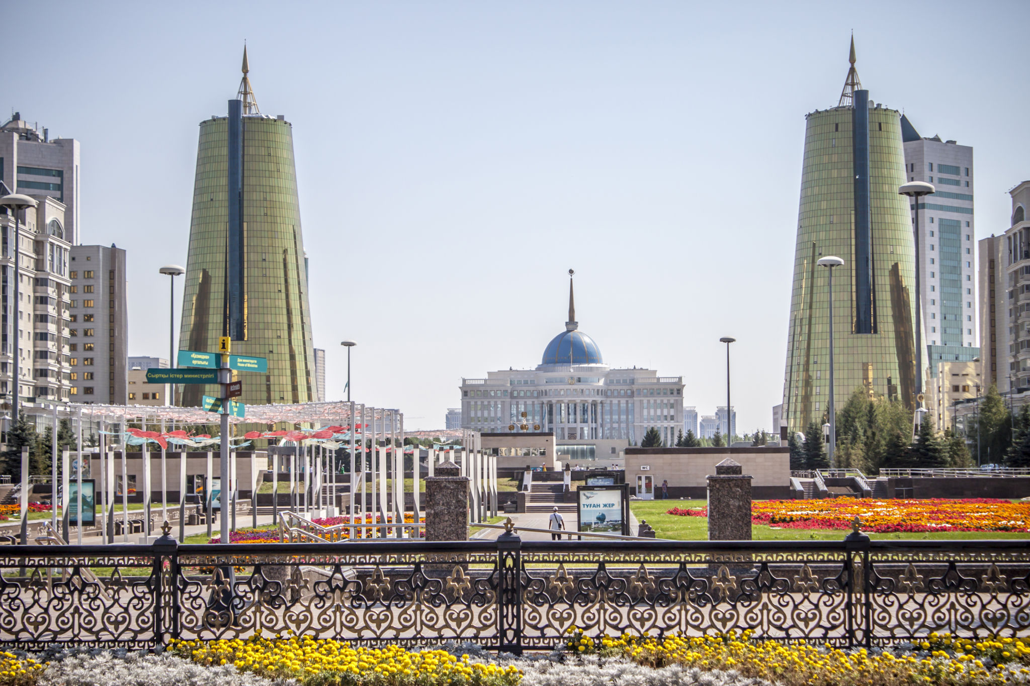 Vy över presidentpalatset i Kazakstan med en gul- och rödblommig parkmiljö i förgrunden och stora torn på sidorna.