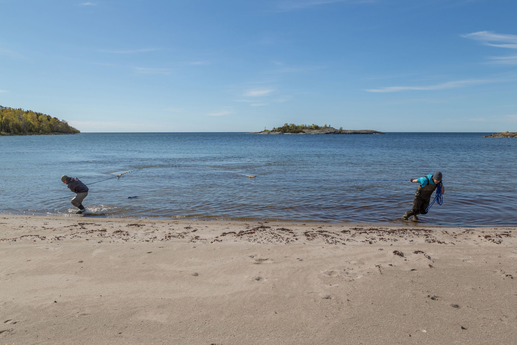 Two men pulling a seine on a sandy beach.
