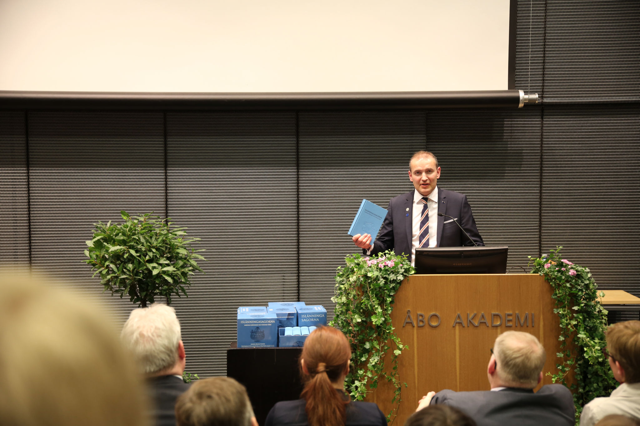 Islands president Guðni Th. Jóhannesson står vid talarpodiet och håller ett exemplar av Islänningasagorna i sin hand.