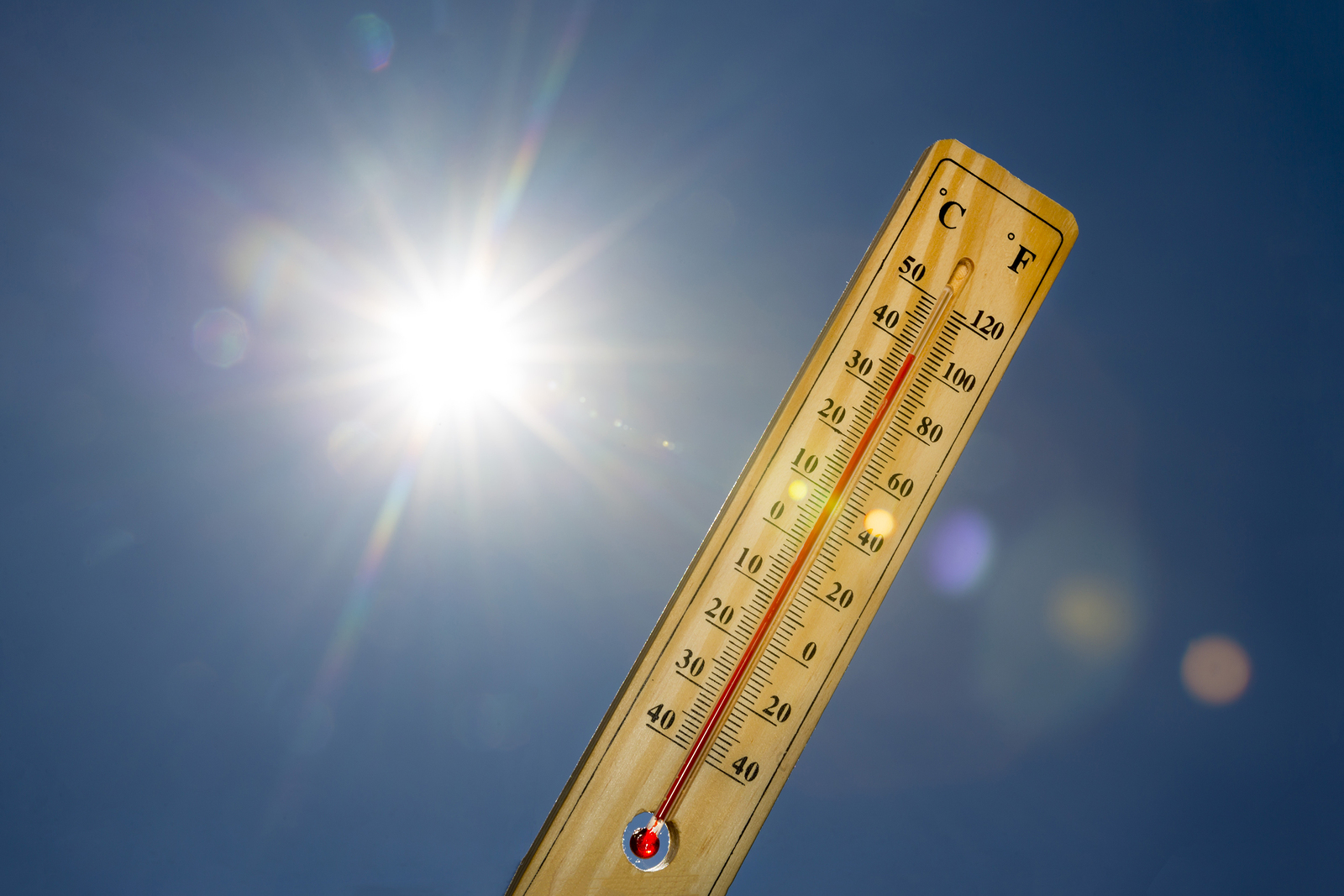 Mercury thermometer marking 39 degrees Celsius 100 Fahrenheit in a sunny day. Summer heat shown on mercury thermometer against the blue sky. Sunlight with sun flares.