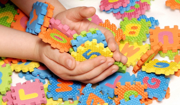 Barnhänder som håller i bokstavs- och sifferpusselbitar.