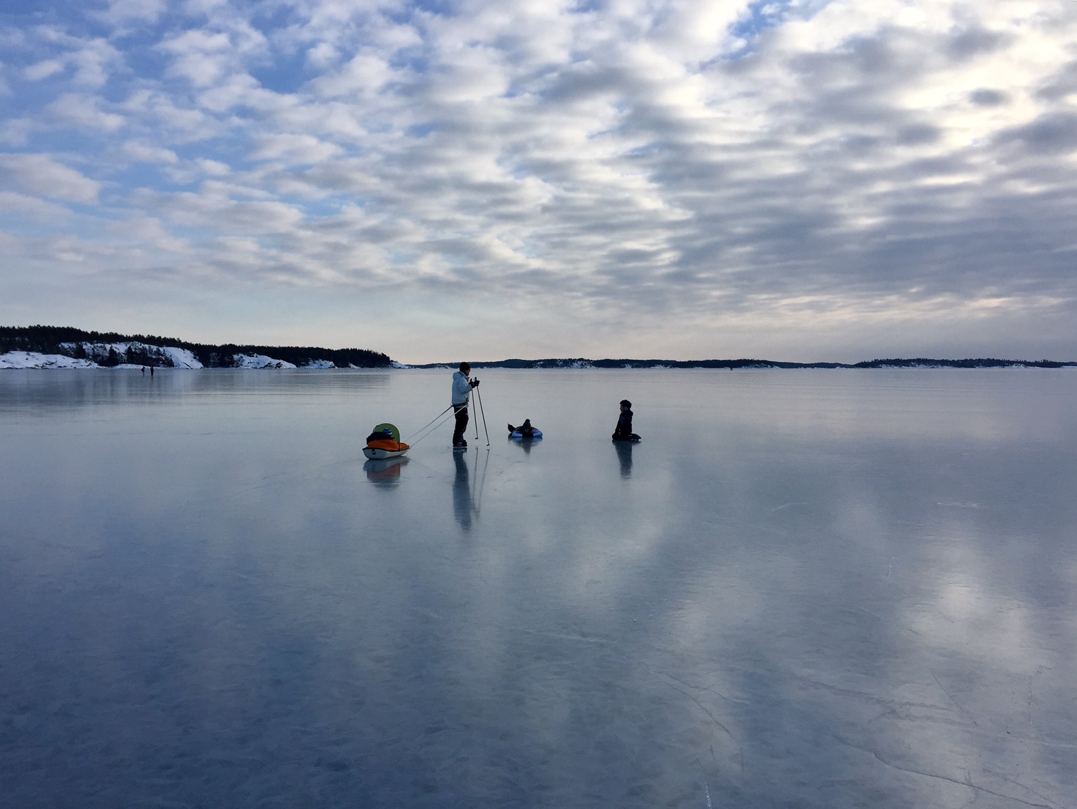 Några personer på spegelblank is med långfärdsskridskor och kälke