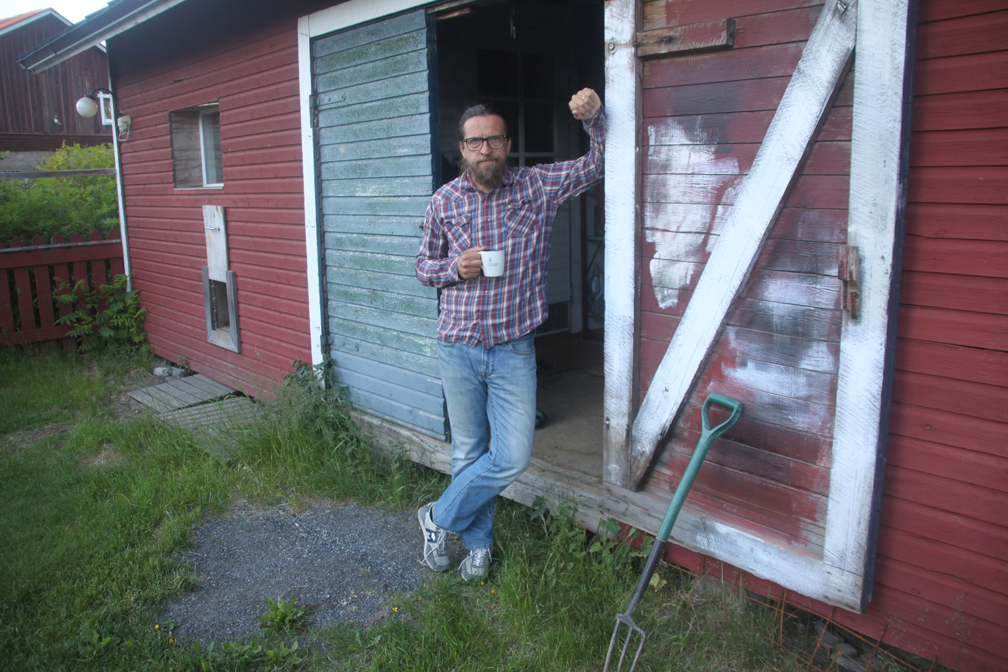 Kai Latvalehto med en kaffemugg i handen vid porten till ett rött uthus.