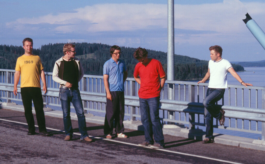 Foto på rockbandet Aknestik, fem män i färggranna skjortor på en bro.