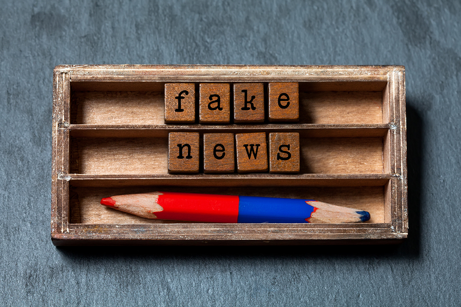 Fake news concept. Vintage box wooden cubes words phrase Fake News old style letters words, red blue pencil on gray stone textured background. Close-up, up view, soft focus.