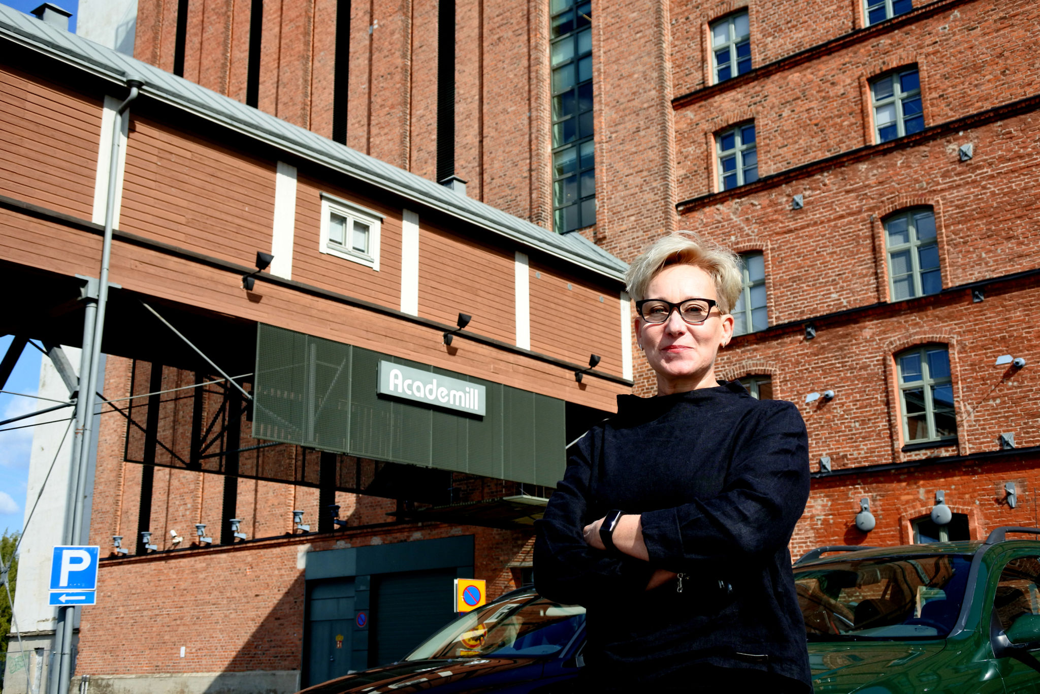 Professor Mia Porko-Hudd, står med armarna i kors framför Academill i Vasa, röd tegelbyggnad.