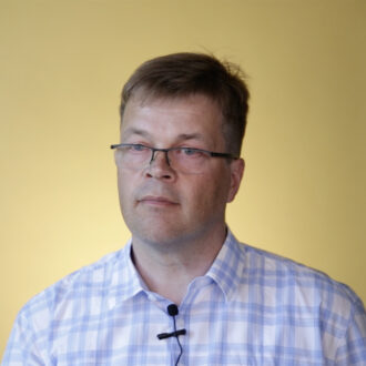 Ronald Österbacka i blåvitrutig skjorta, framför gul bakgrund.