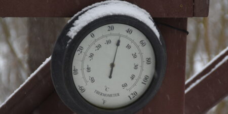 Round Circular Outdoor Thermometer covered with snow shows low temperatures near zero. Low temperatures in degrees Celsius and fahrenheit. Cold winter weather - zero celsius thirty two farenheit