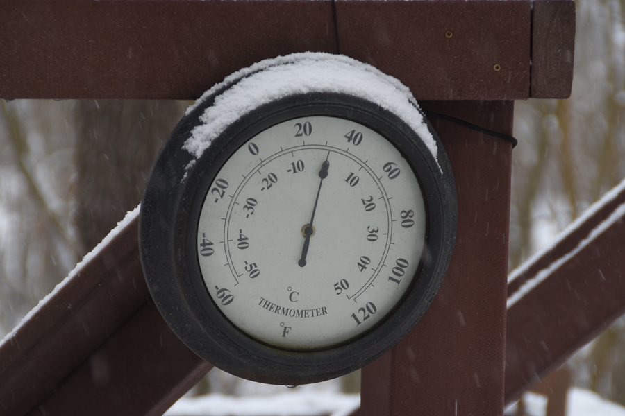 Round Circular Outdoor Thermometer covered with snow shows low temperatures near zero. Low temperatures in degrees Celsius and fahrenheit. Cold winter weather - zero celsius thirty two farenheit
