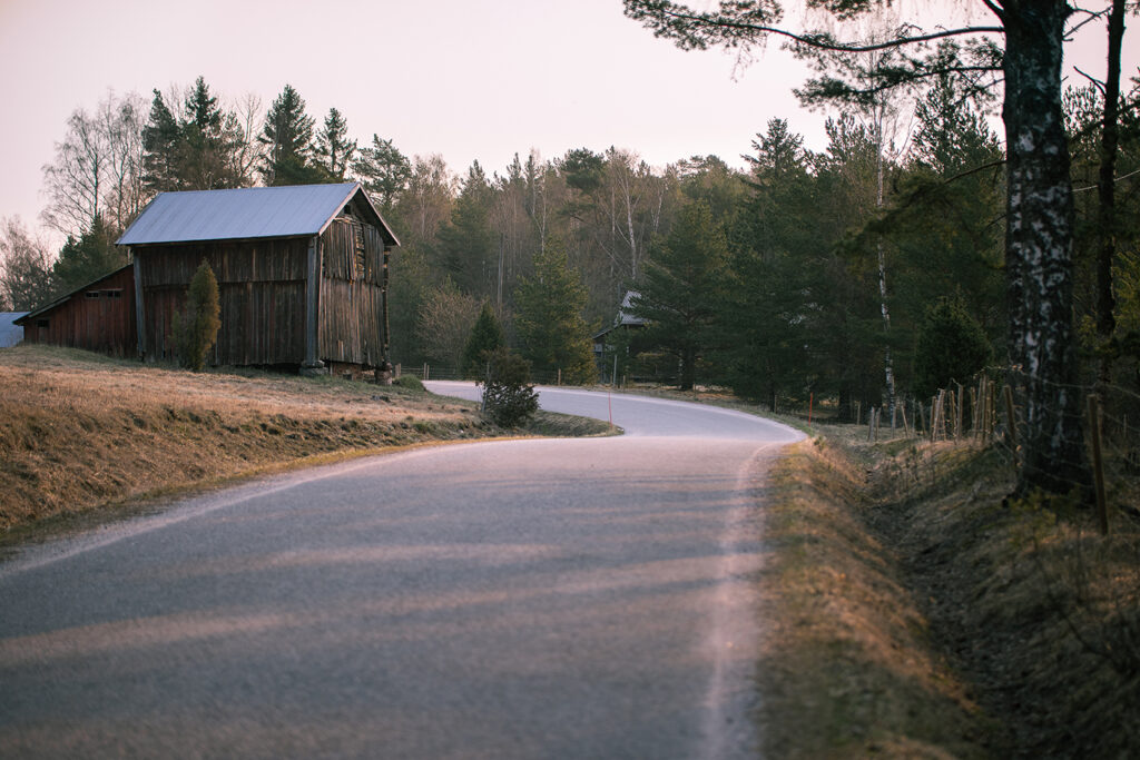 Asfalterad väg slingrar sig ut bakom en lada med skog i bakgrunden.