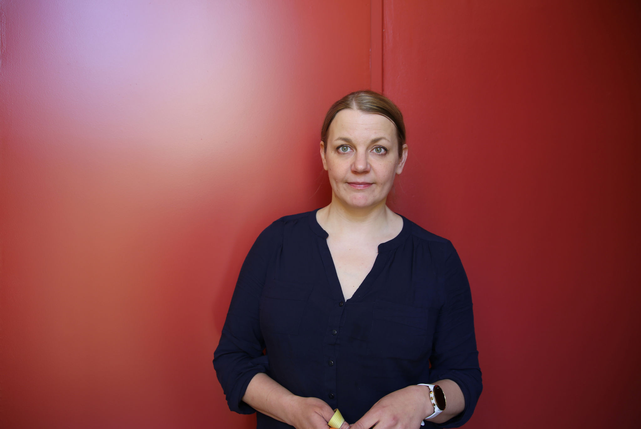Forskare Nina Tynkkynen står framför en röd vägg.