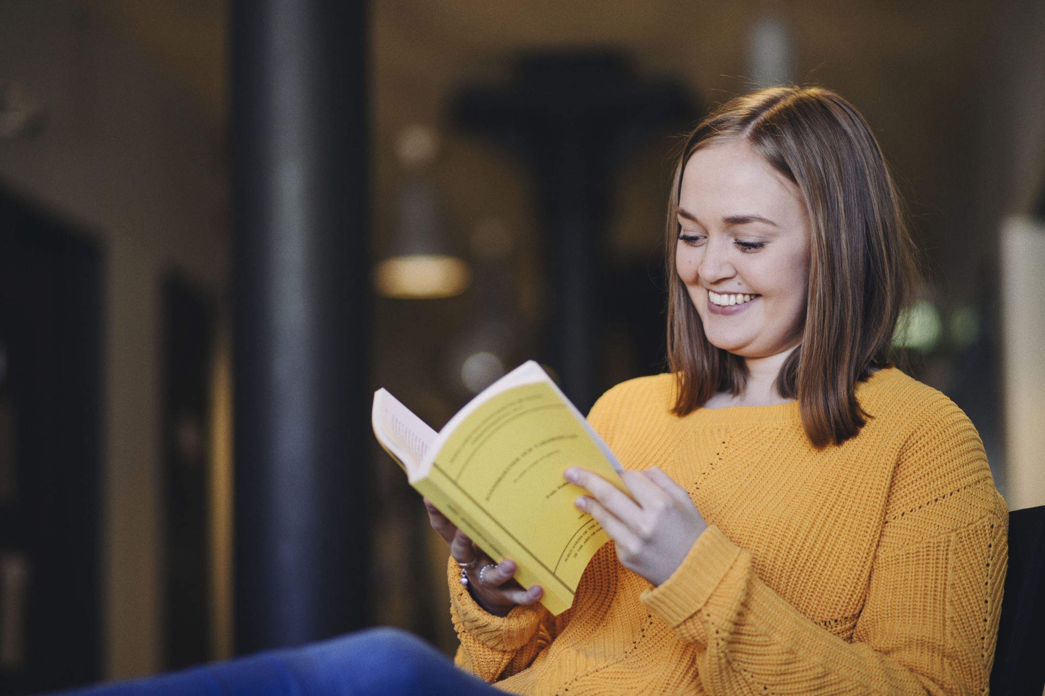 Kvinna i gul blus läser en gul bok.