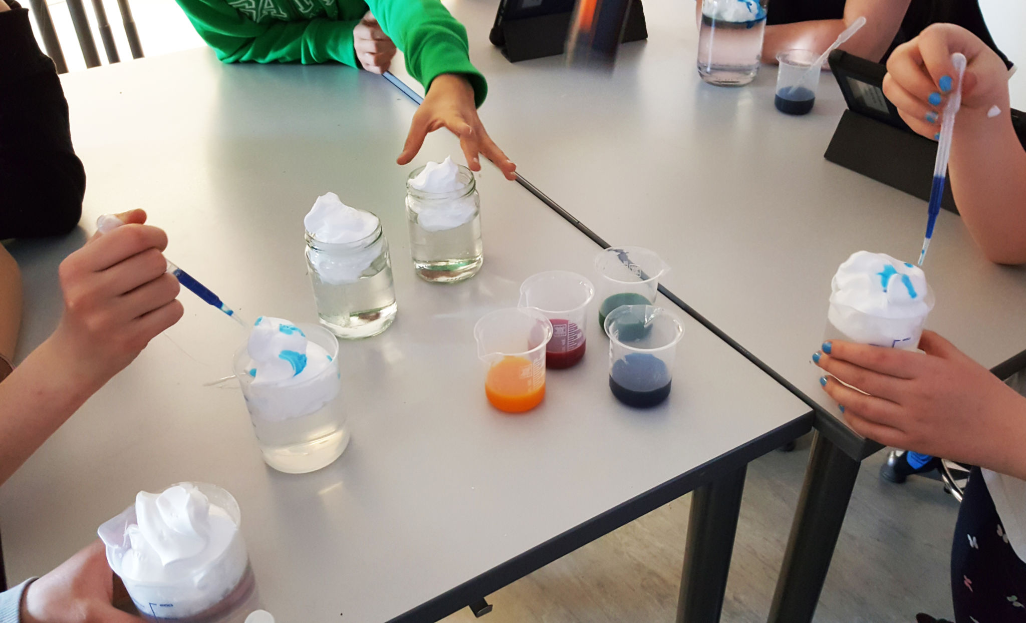 Barnhänder använder pipetter, glaskärl och färggranna vätskor för kemitester.