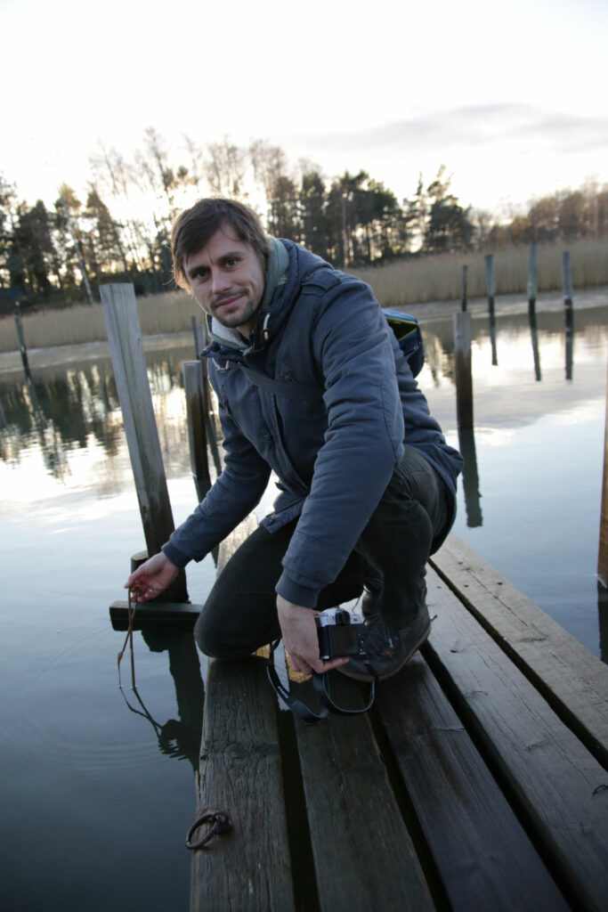 Christian Pansch kneeling on a wharf with the sea in the background.