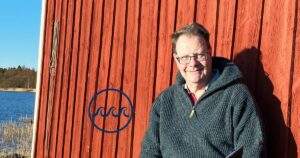 Marko Joas sitter framför en röd fiskestuga vid havet