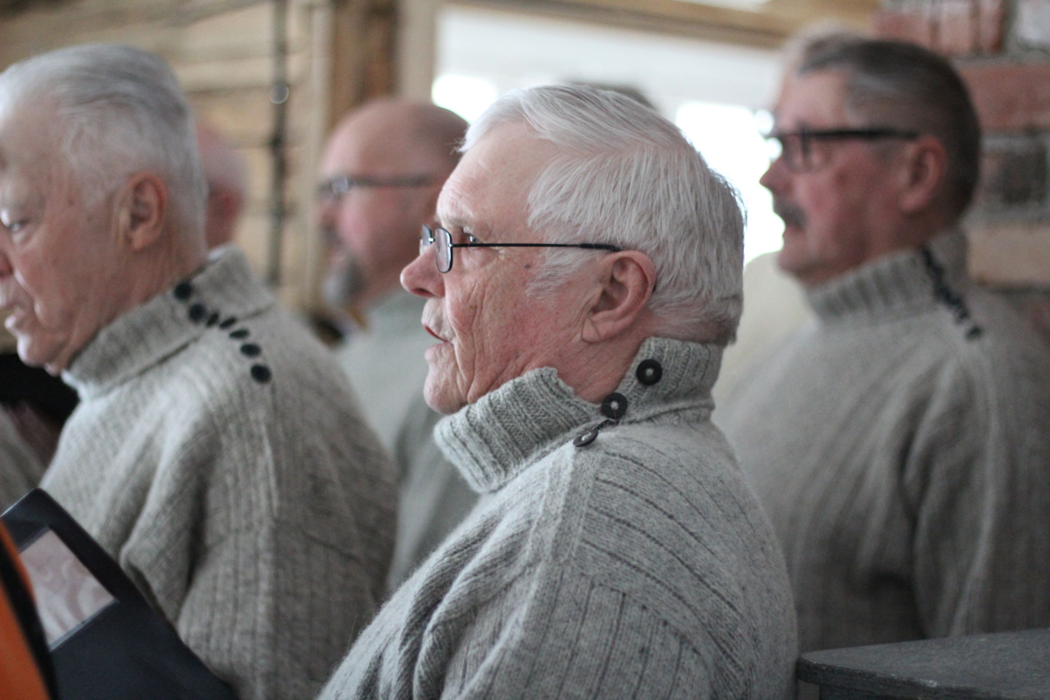 En man i profil med grå stickatröja på sig. Han sjunger i kör.