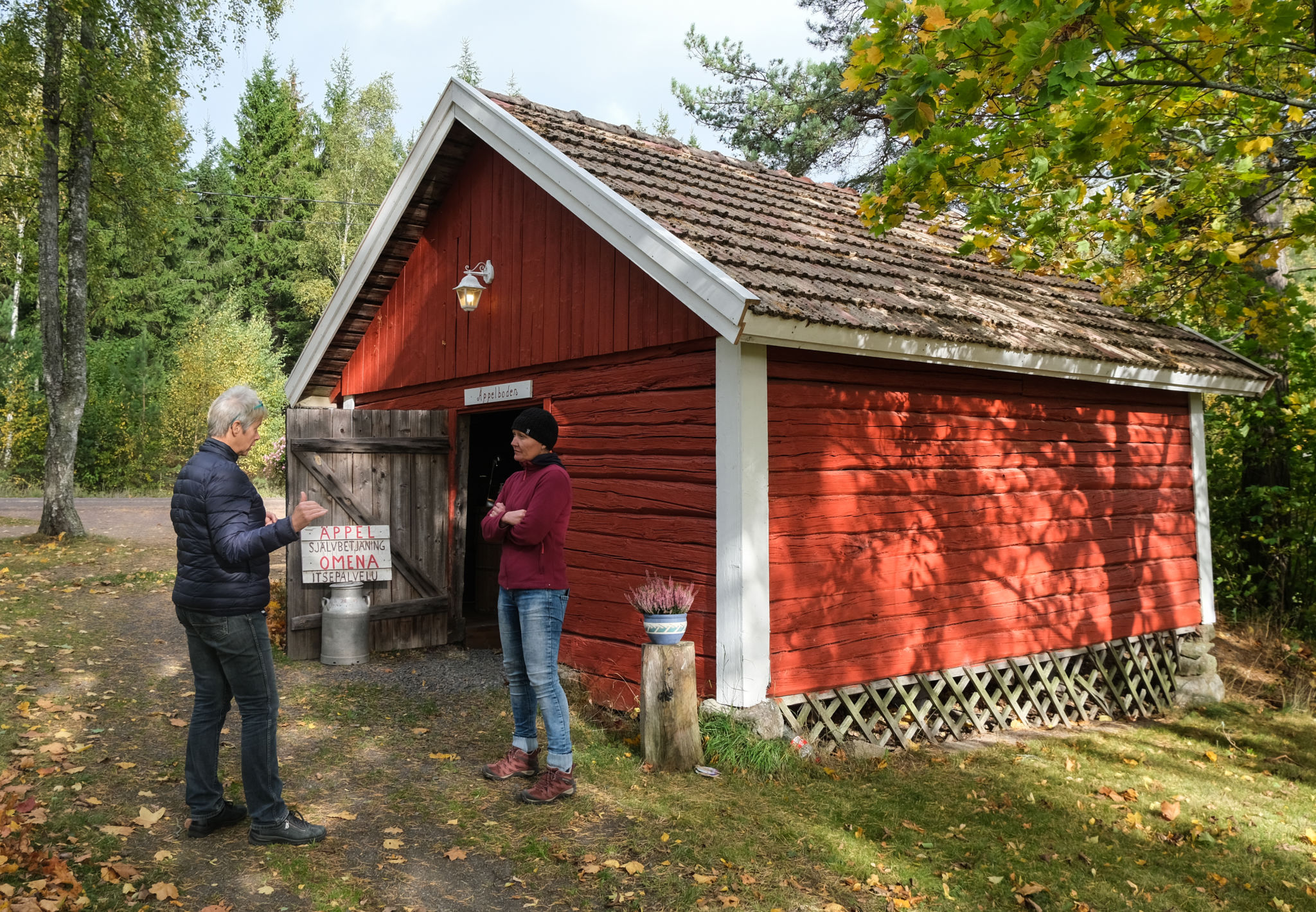 Två kvinnor utanför en rödmålad gammal bod.