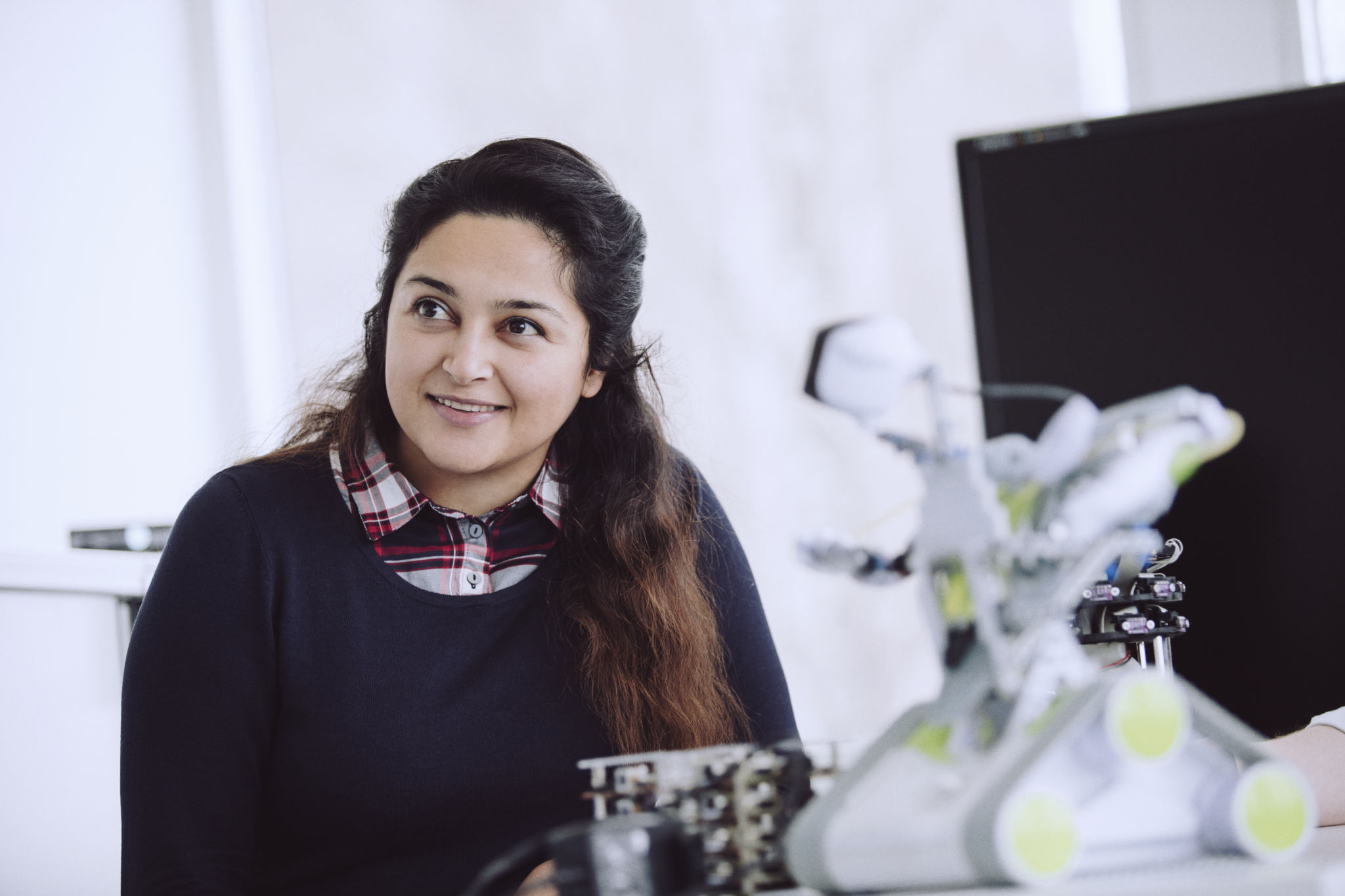 Studerande som sitter och ler med en robot på ett bord framför sig.