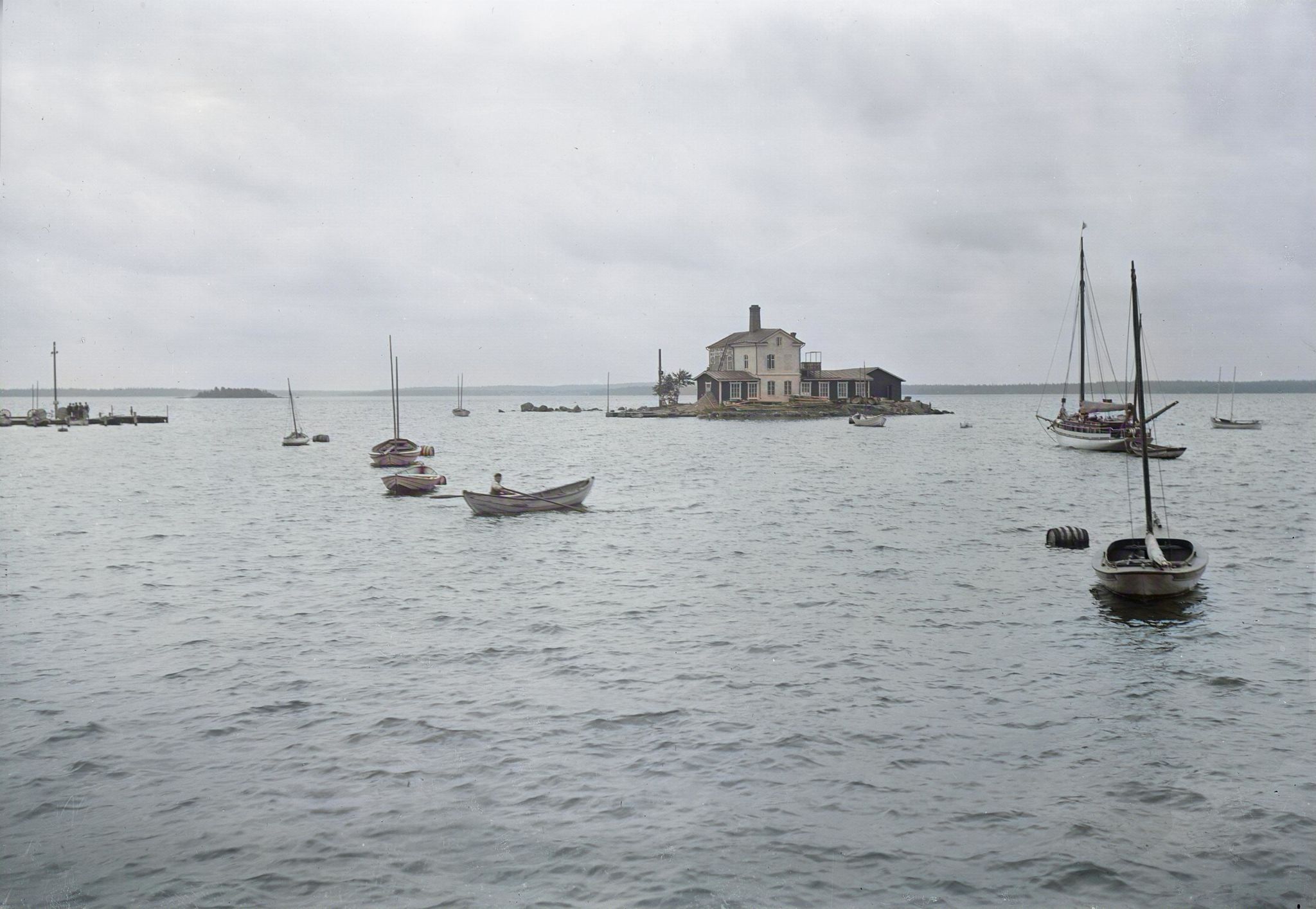 Många mindre båtar till havs kring en liten ö med ett hus på.