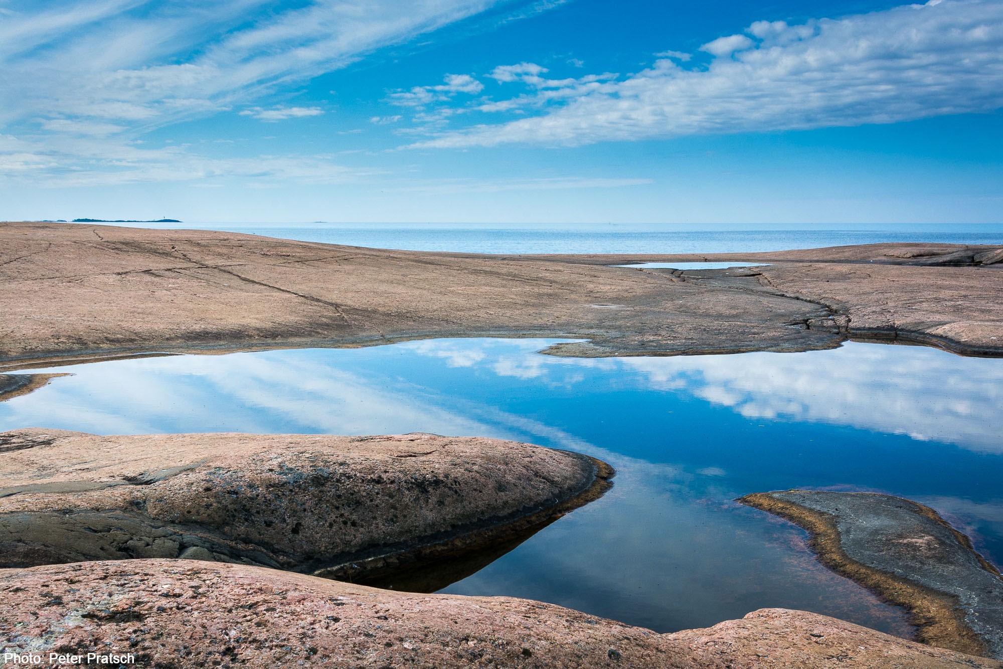 Klippö med himmel reflekterande vatten