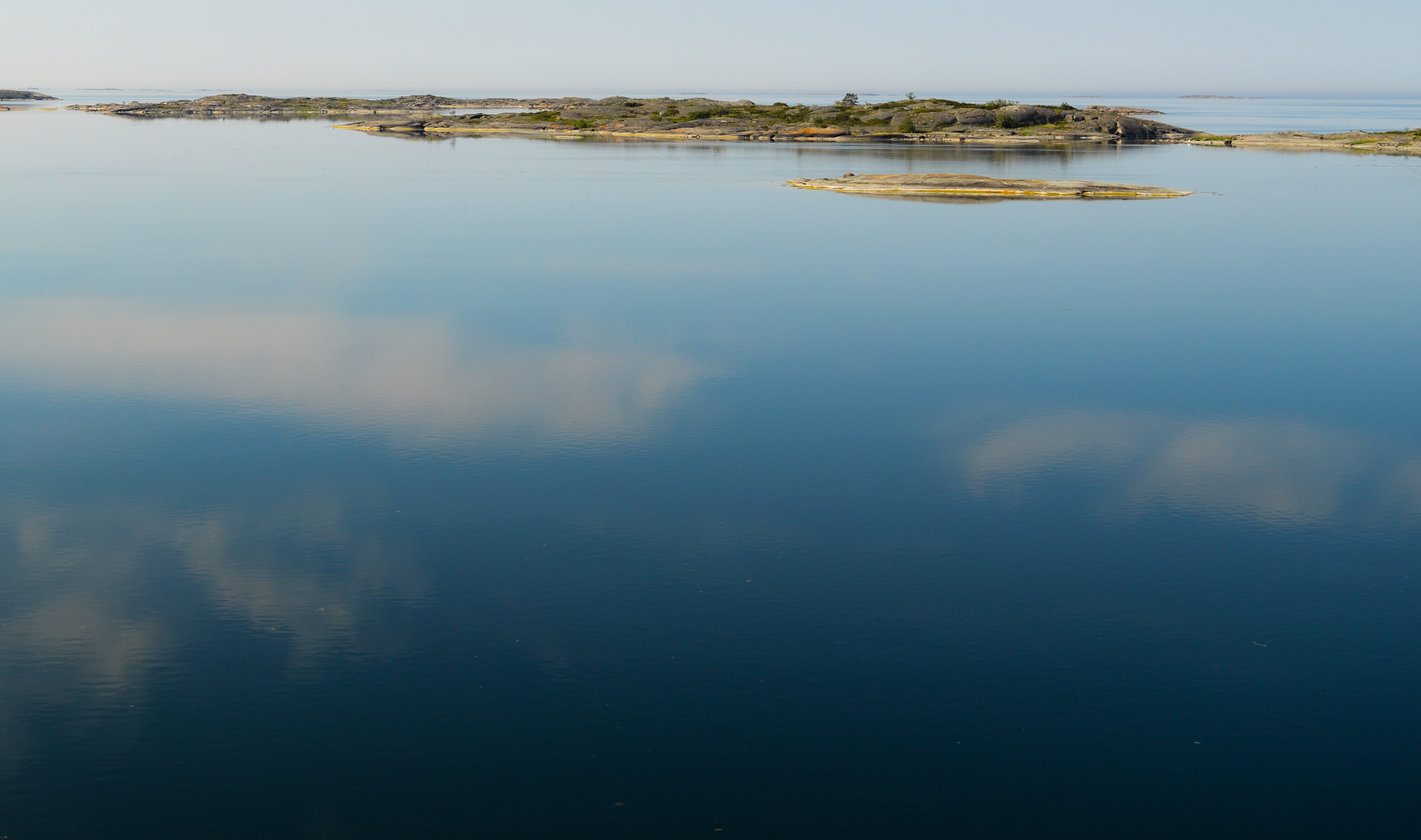 Ett spegelblankt hav en solskensdag. I horisonten ses små öar.