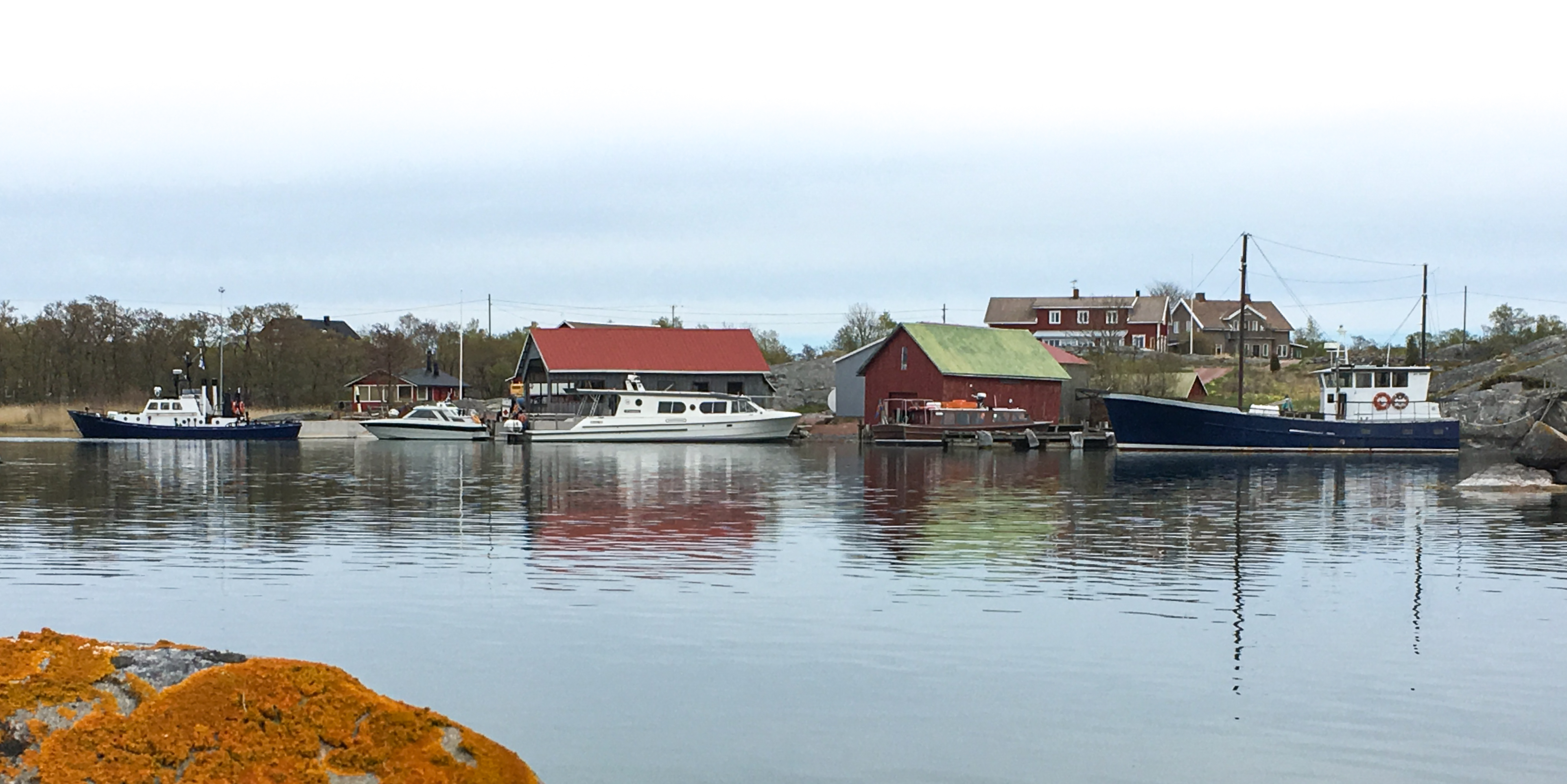 Vy från havet över hamnen på Kyrkogårdsö. Några båthus och båtar.