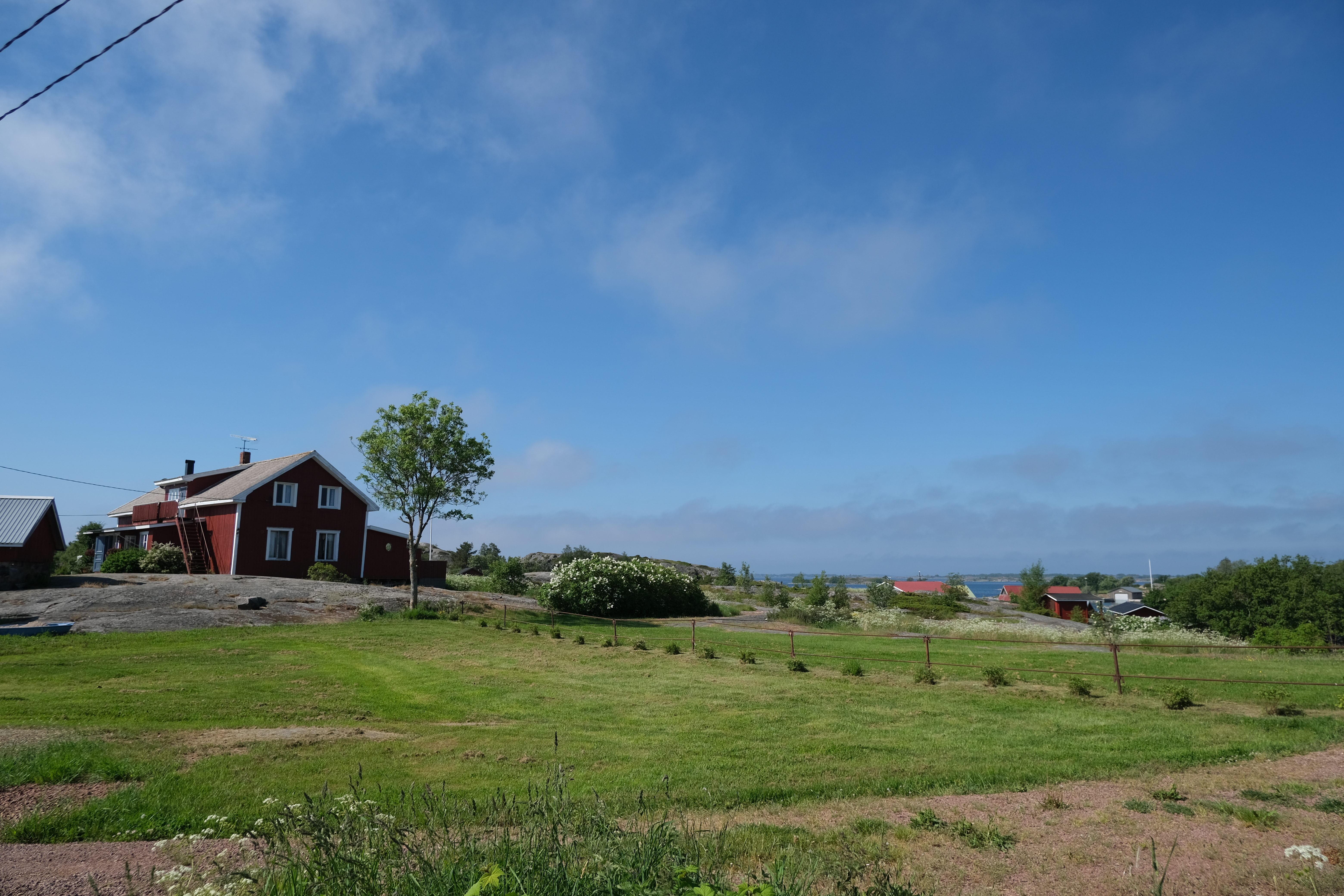 Sommarvy från en skärgårdsö. Rött hus, gröna ängar och öppet hav.