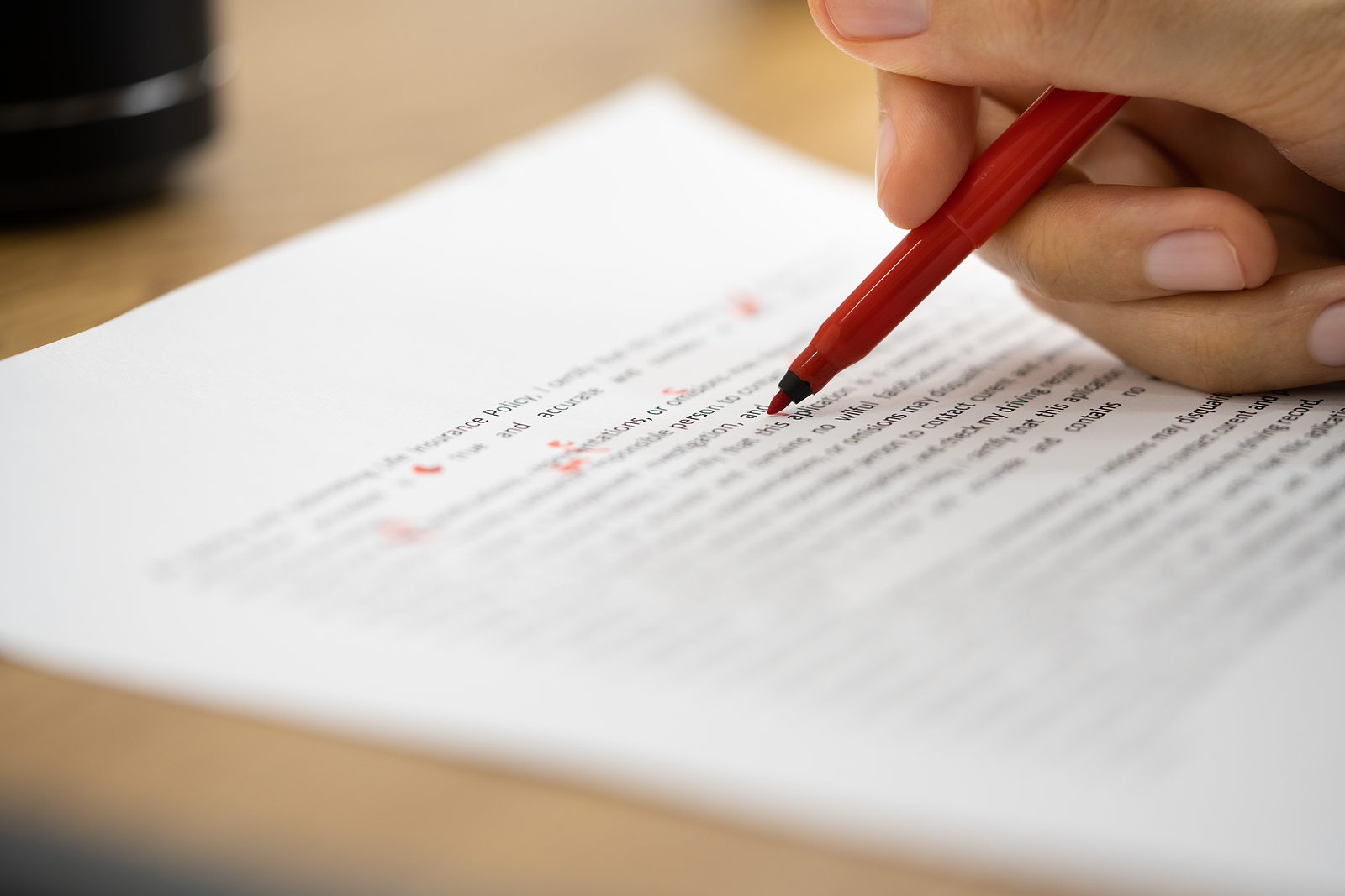 En röd penna markerar på ett papper med text.