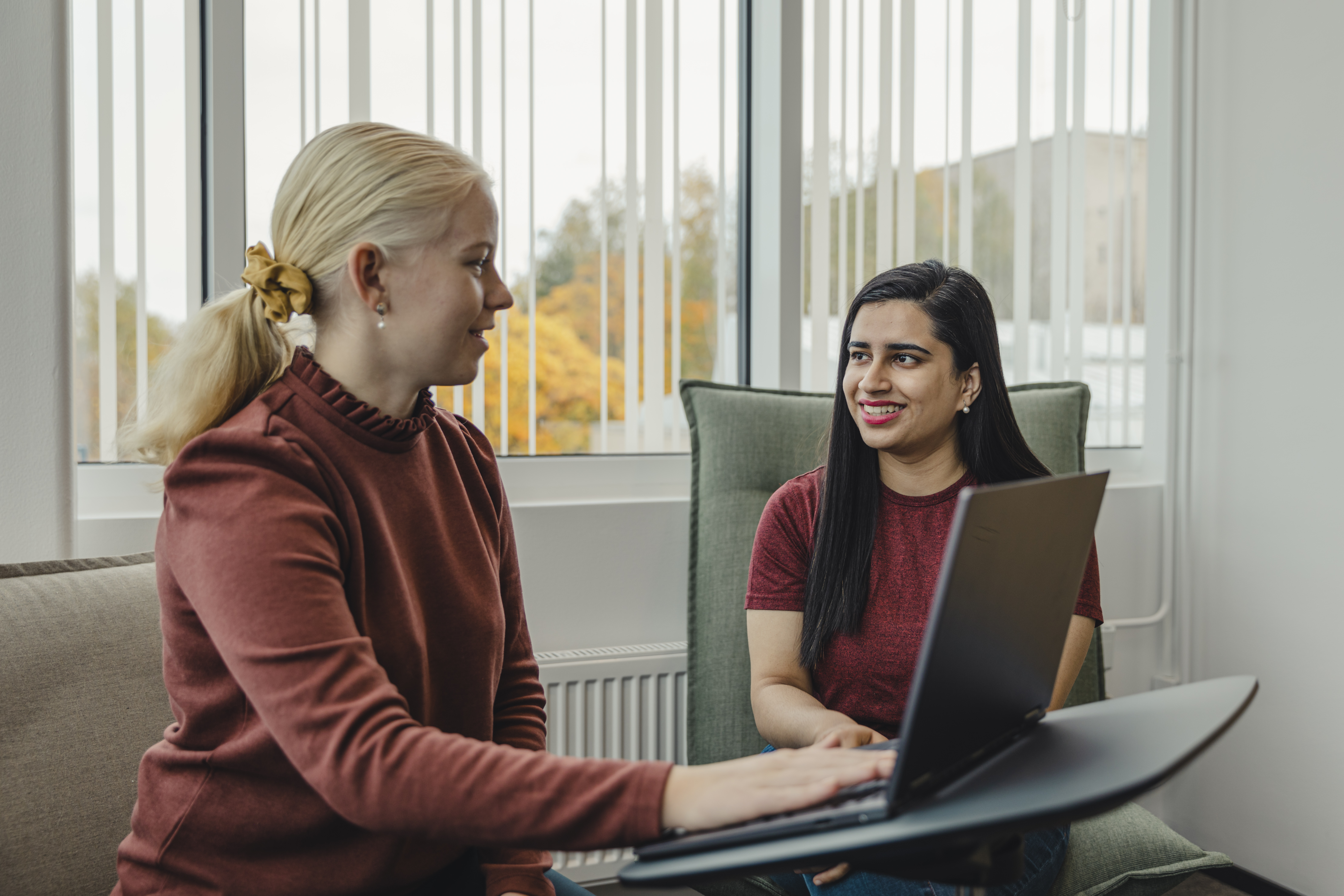 Två kvinnor diskuterar och ler i ett grupprum med en dator.