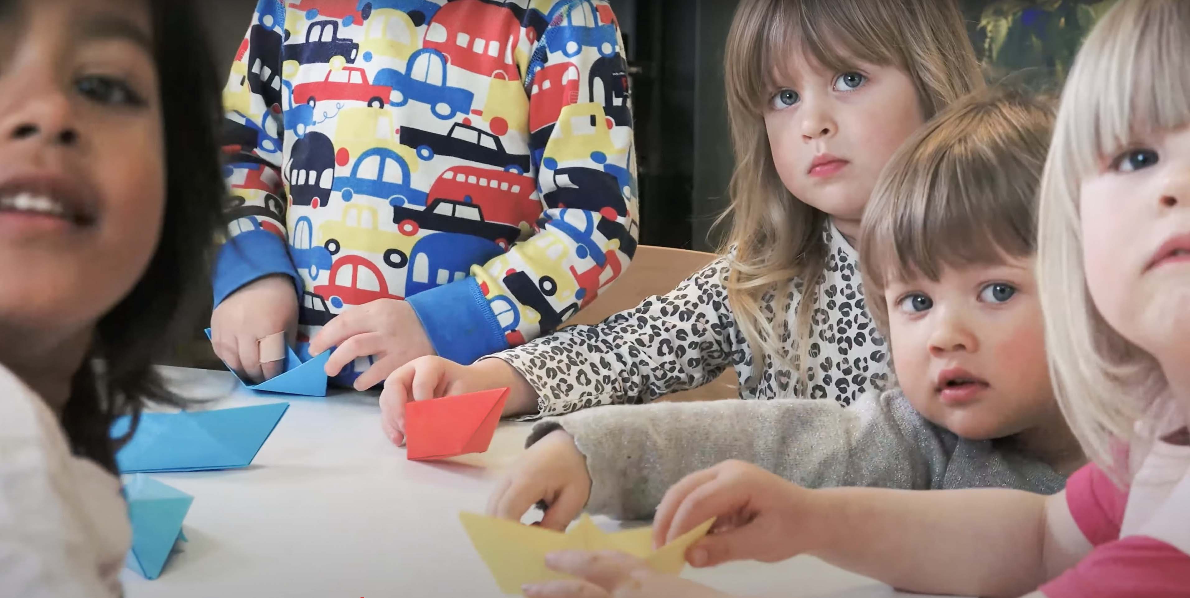 Barn viker pappersgrejer runt ett bord.