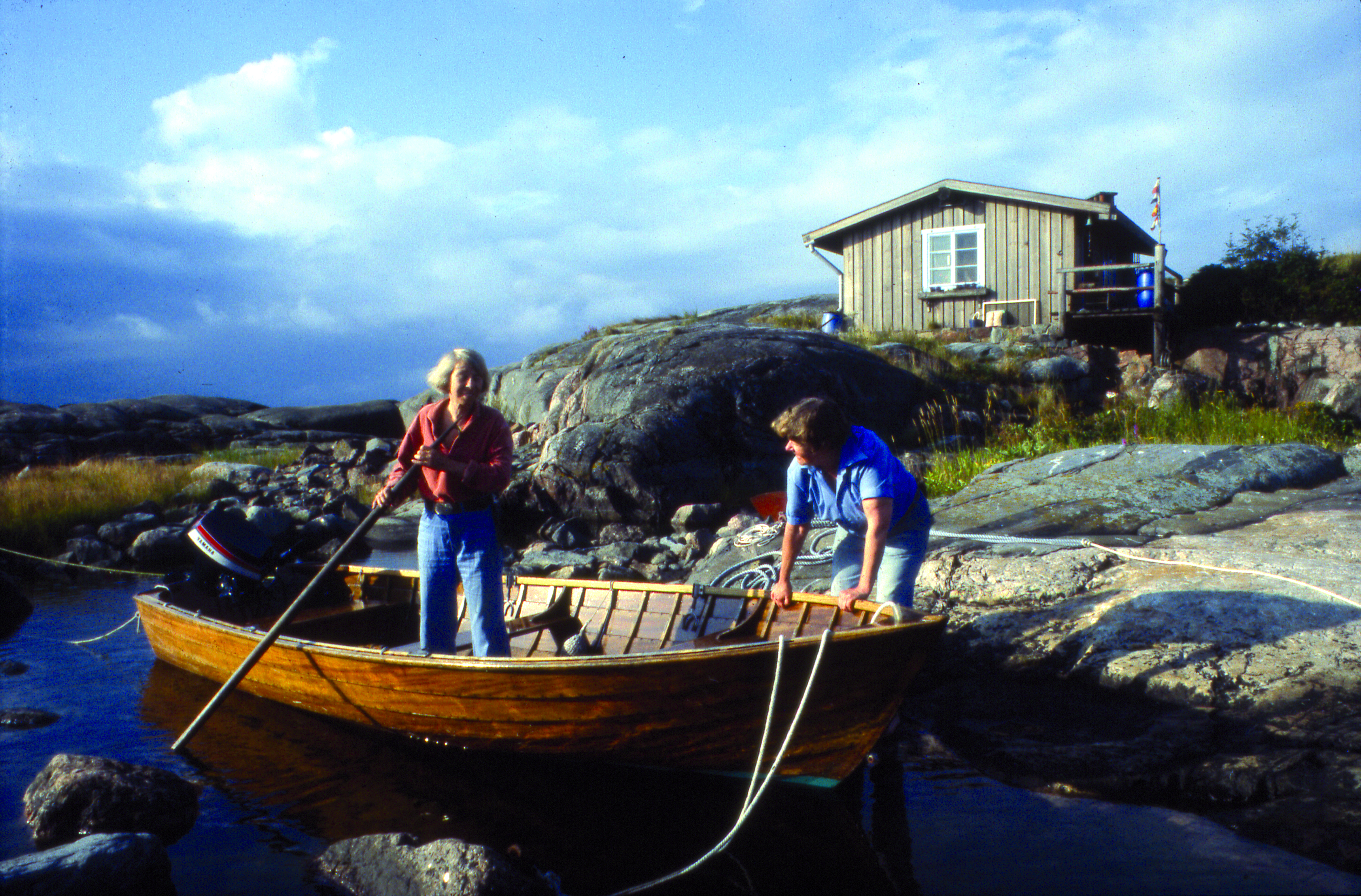 Två kvinnor vadar i strandvattnet vis en roddbåt.