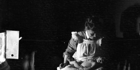 En mörk, svartvit gammal bild på en kvinna med en baby i famnen.