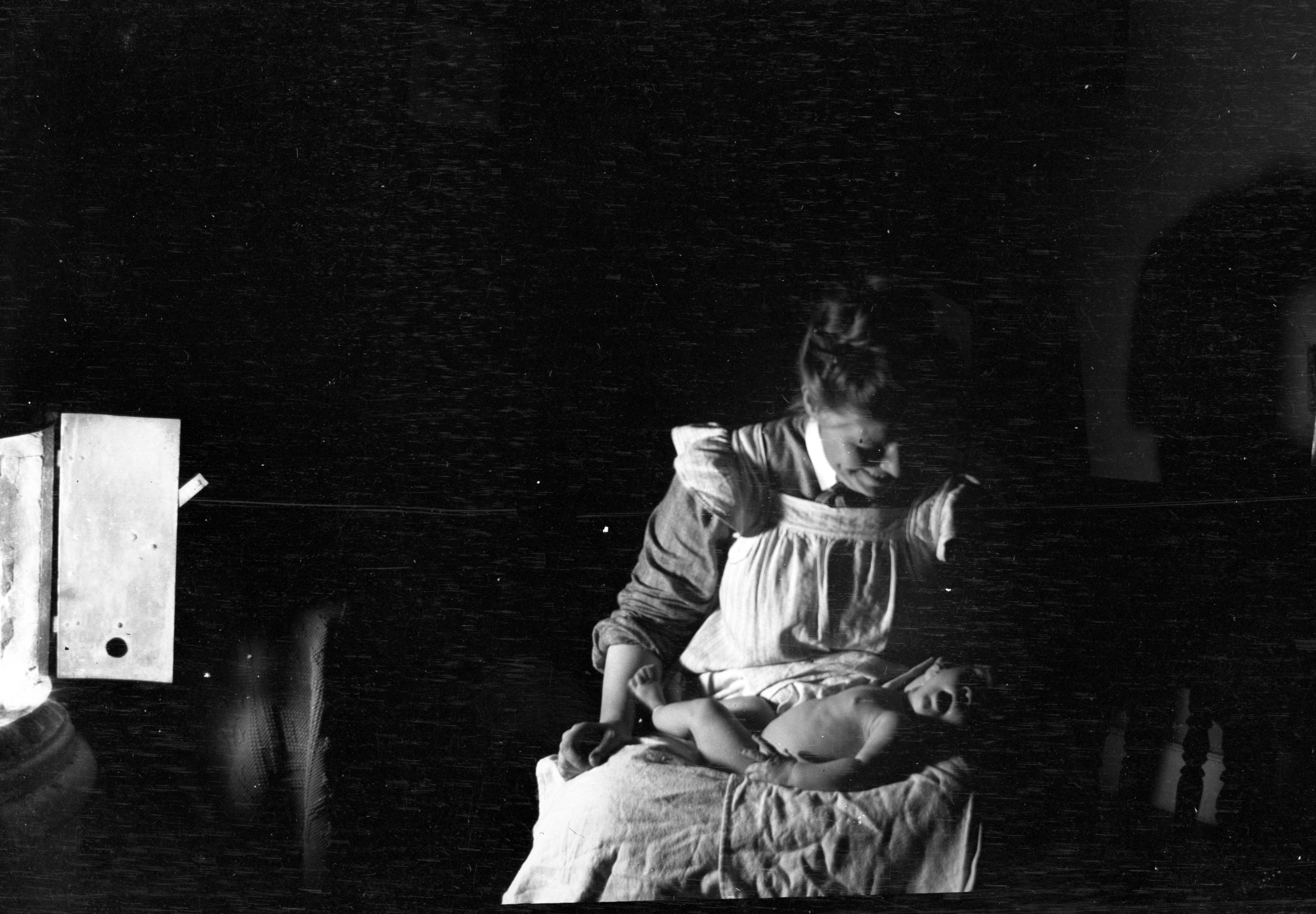 En mörk, svartvit gammal bild på en kvinna med en baby i famnen.
