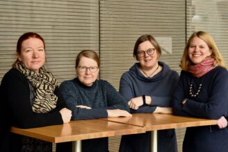 Fyra glada kvinnor står runt ett högt bord.