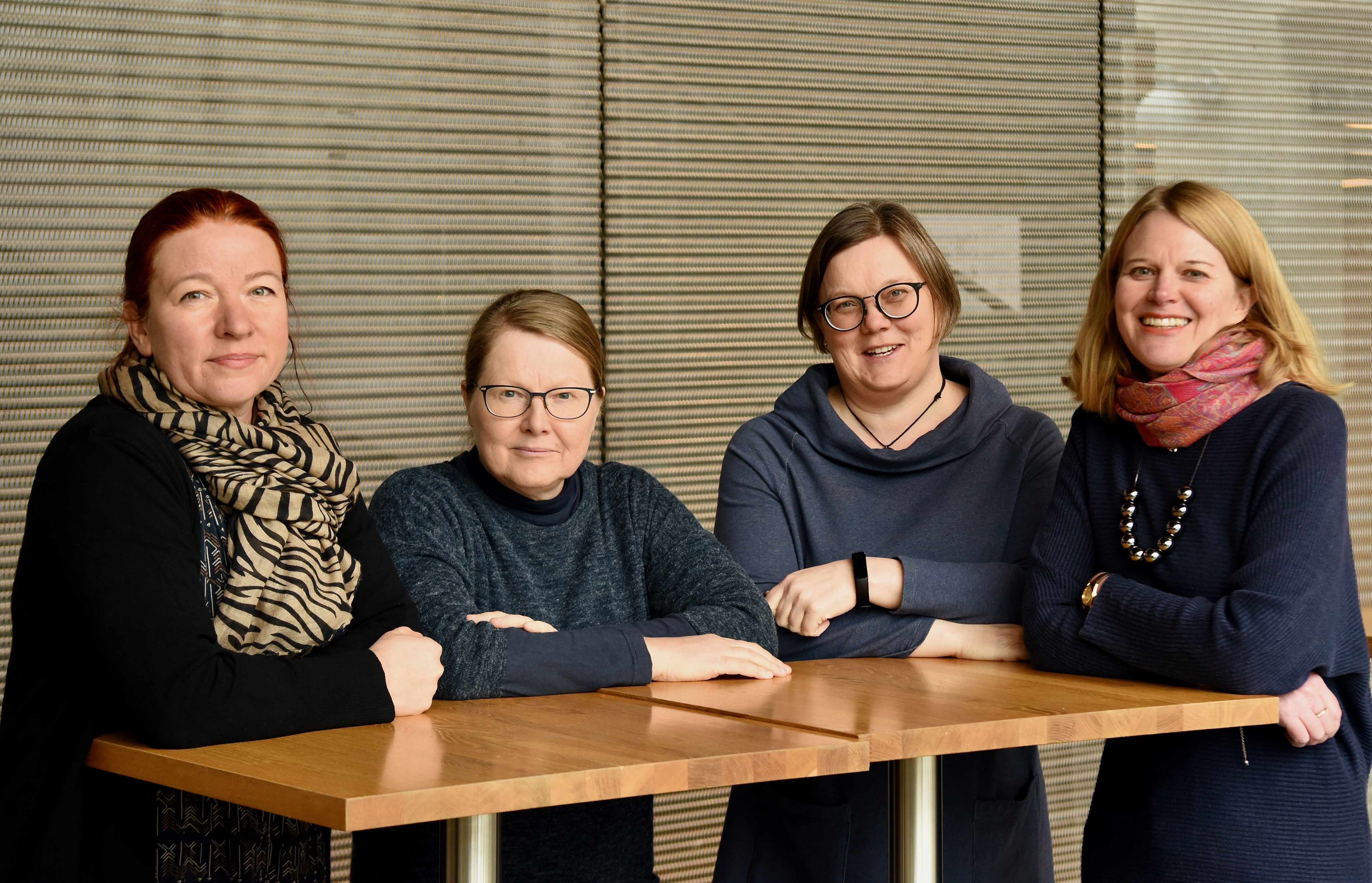 Fyra glada kvinnor står runt ett högt bord.