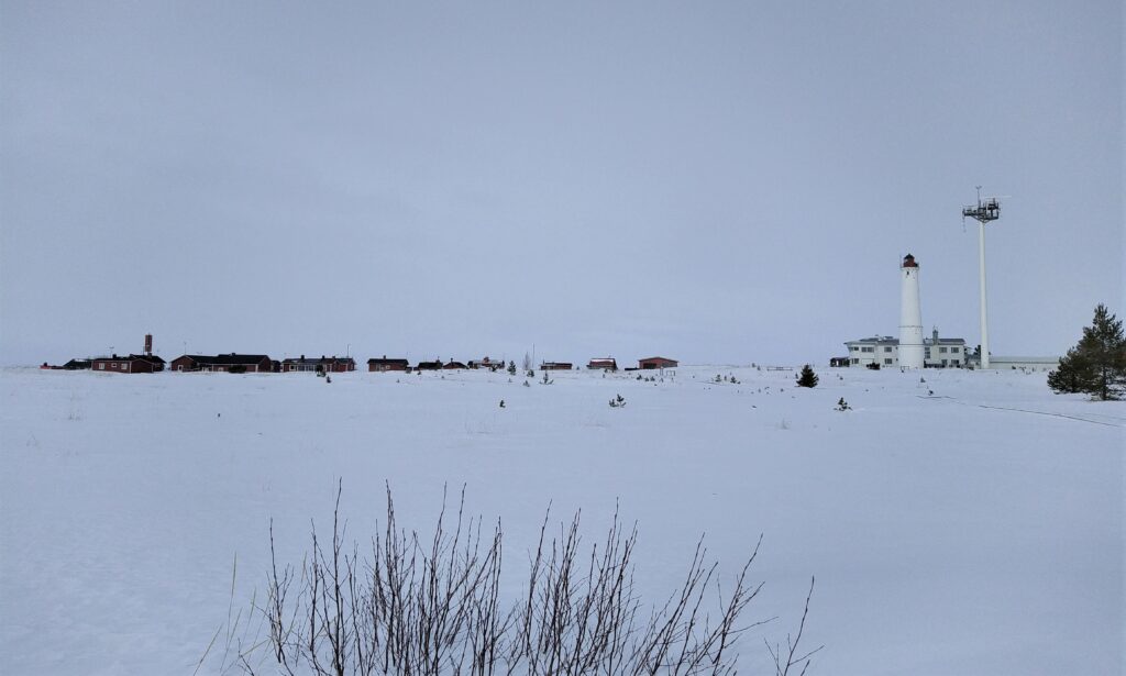 Ett vitt, snöigt landskap med små röda hus och en vit fyr längre i bakgrunden.