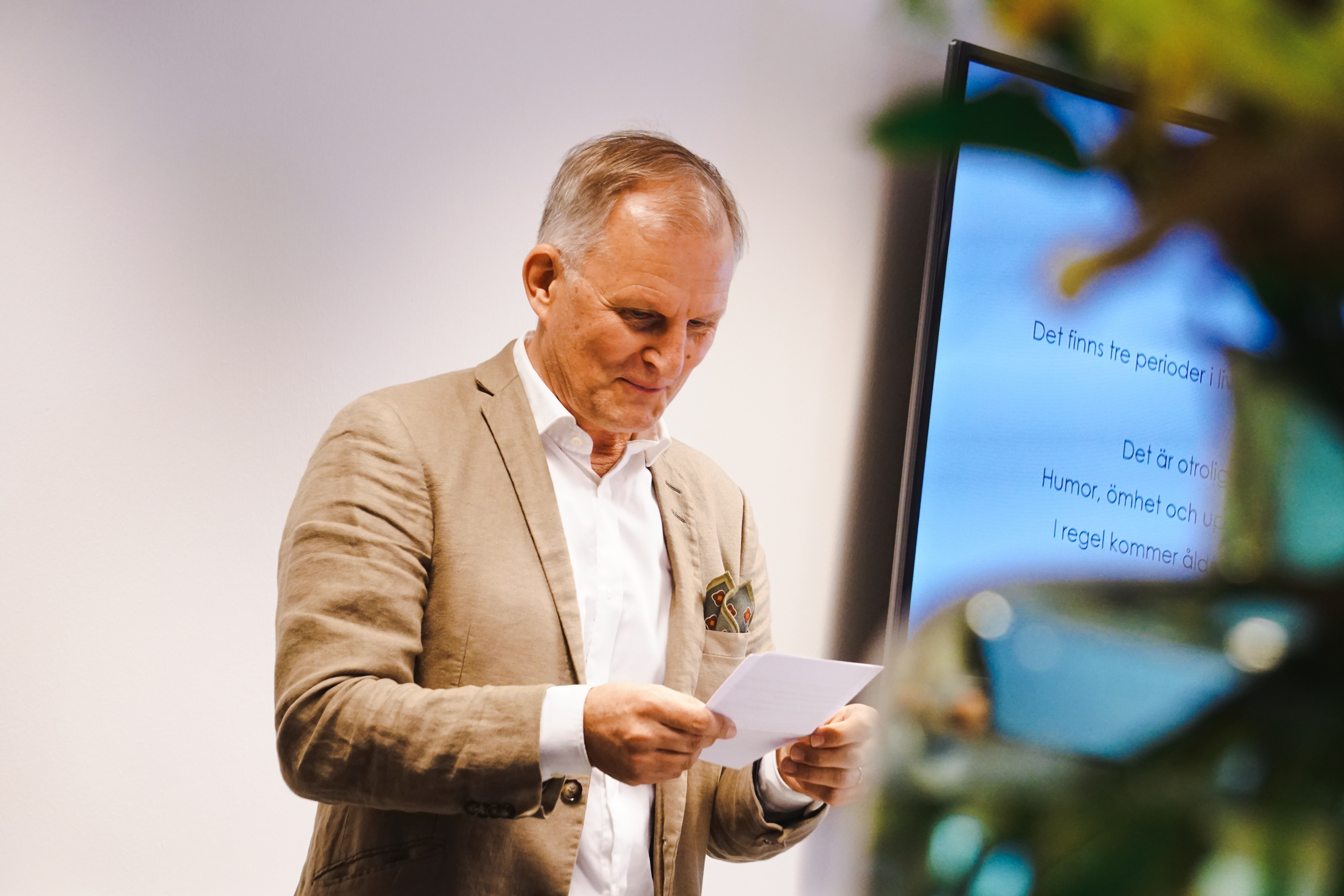 EN skrattande Torbjörn Sandén tittar ner i ett papper och håller tal.