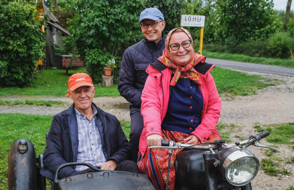 Three smiling people on a motorcykle with a side wagon.