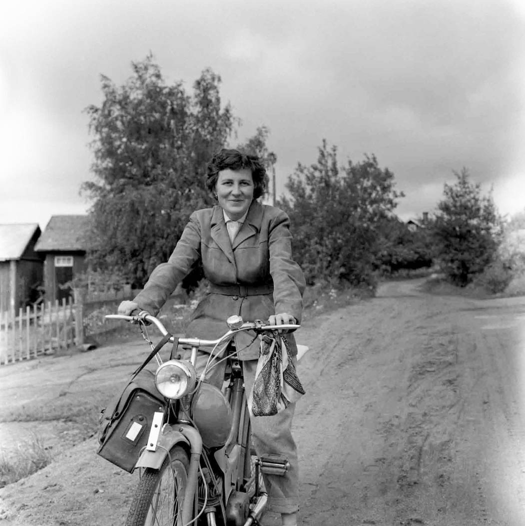 Svart-vit bild från 50-talet på en leende kvinna på moped.