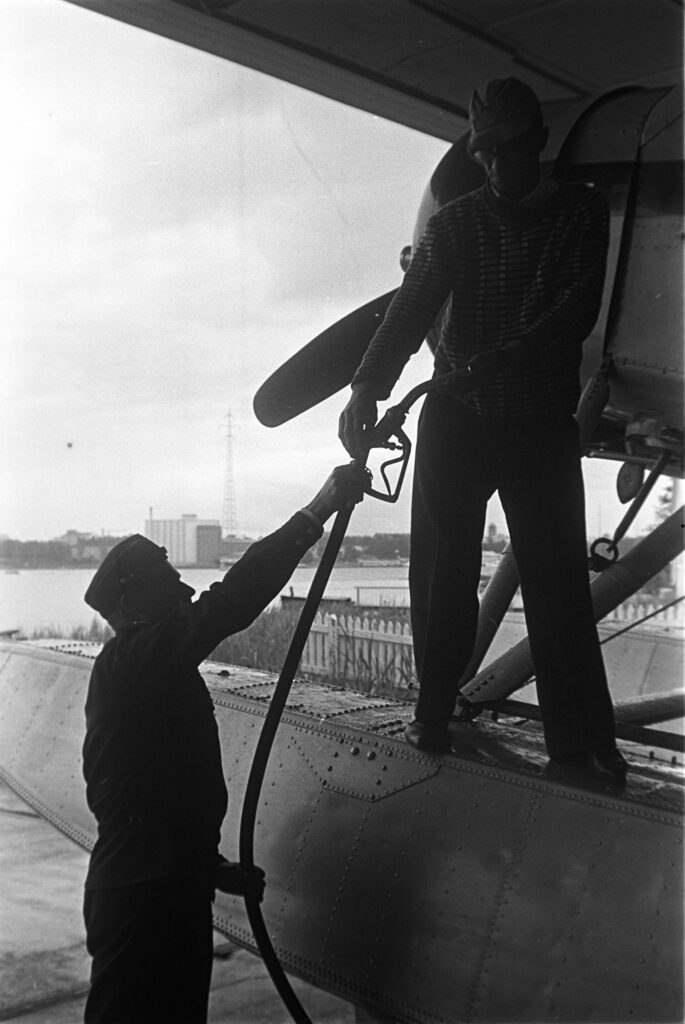 Gammal svartvit bild på två män som tankar ett propellerplan.