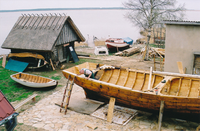 En träbåt i förgrunden, bakom finns vatten och en liten stuga.