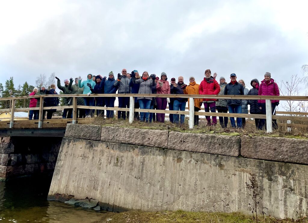 Gruppbild på cirka 30 personer ssom står på en gammal stenbro.