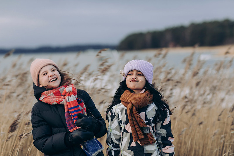 Två glada flickor ute i vintrigt strandlandskap.