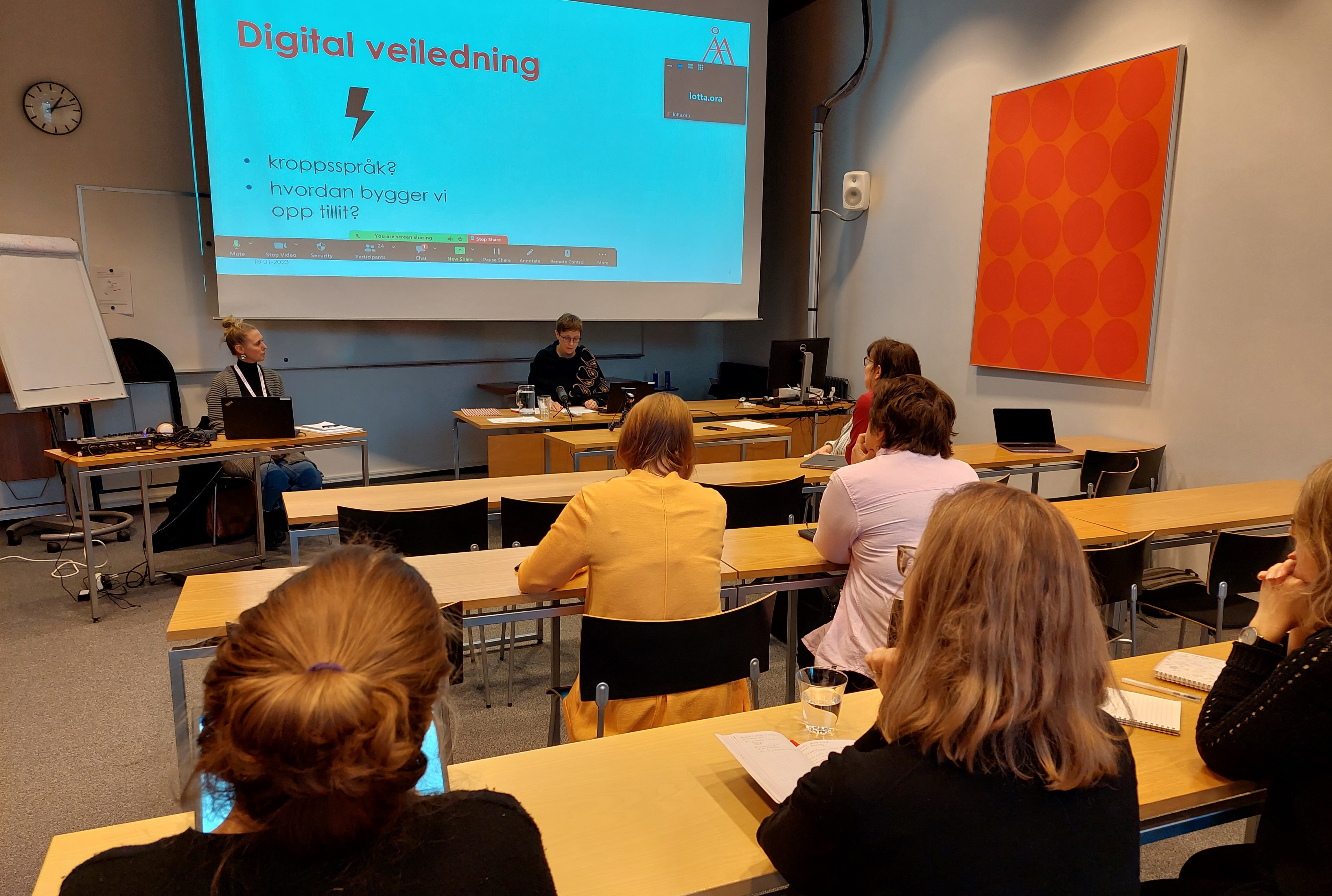 En föreläsningssal med några personer i, fotad bakirgån.