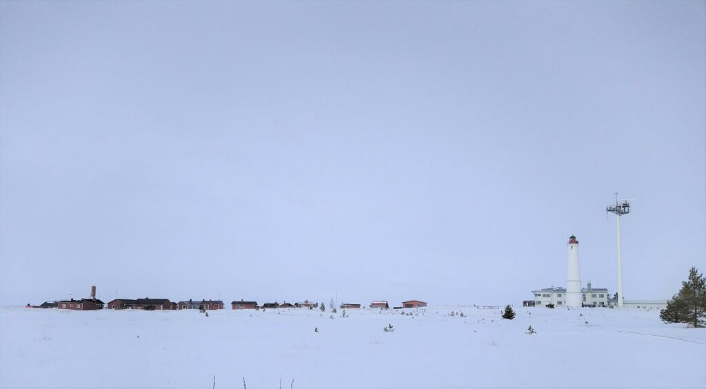 En väldigt snövit vy över en vit fyr. Längre bort syns små stugor.