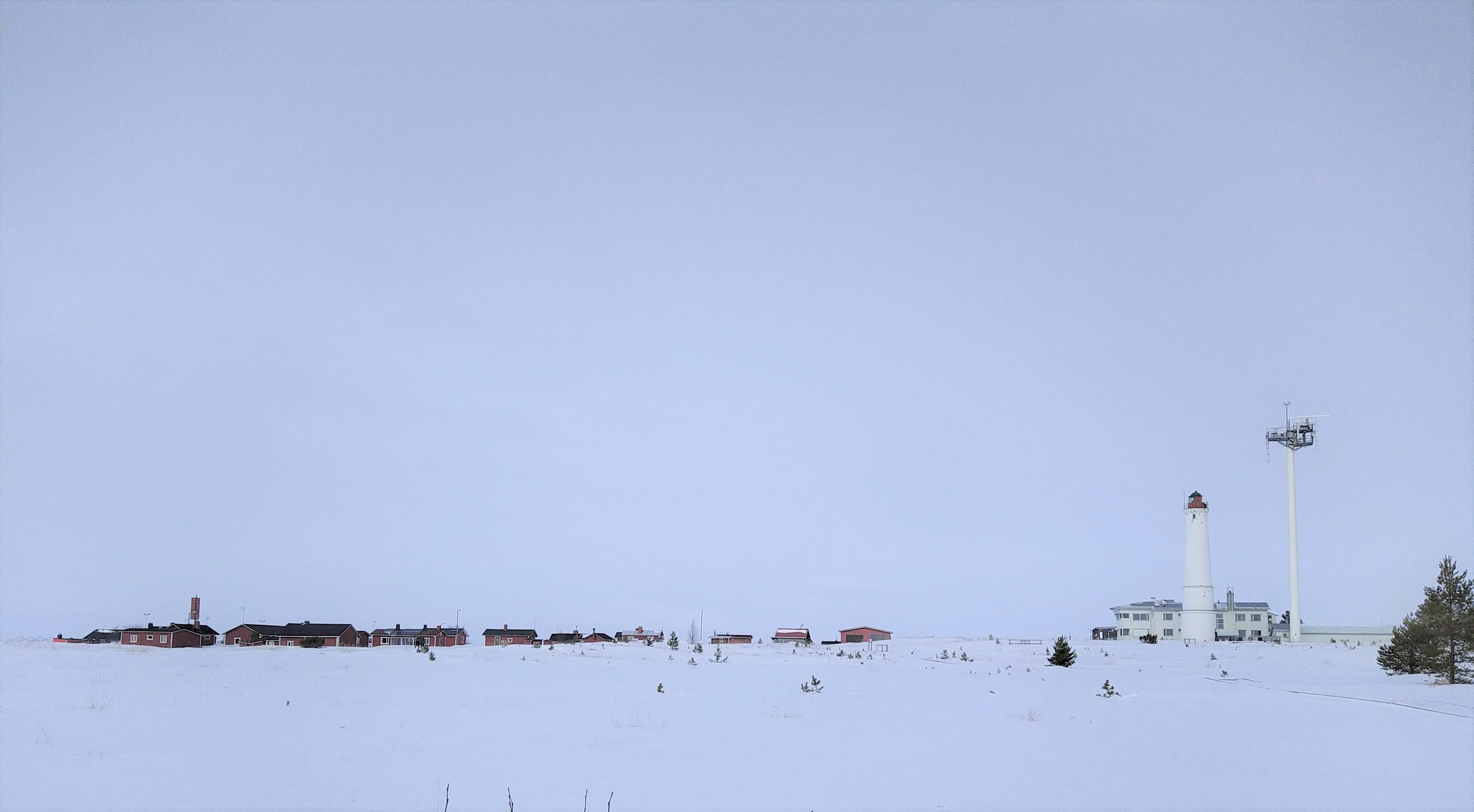 En väldigt snövit vy över en vit fyr. Längre bort syns små stugor.