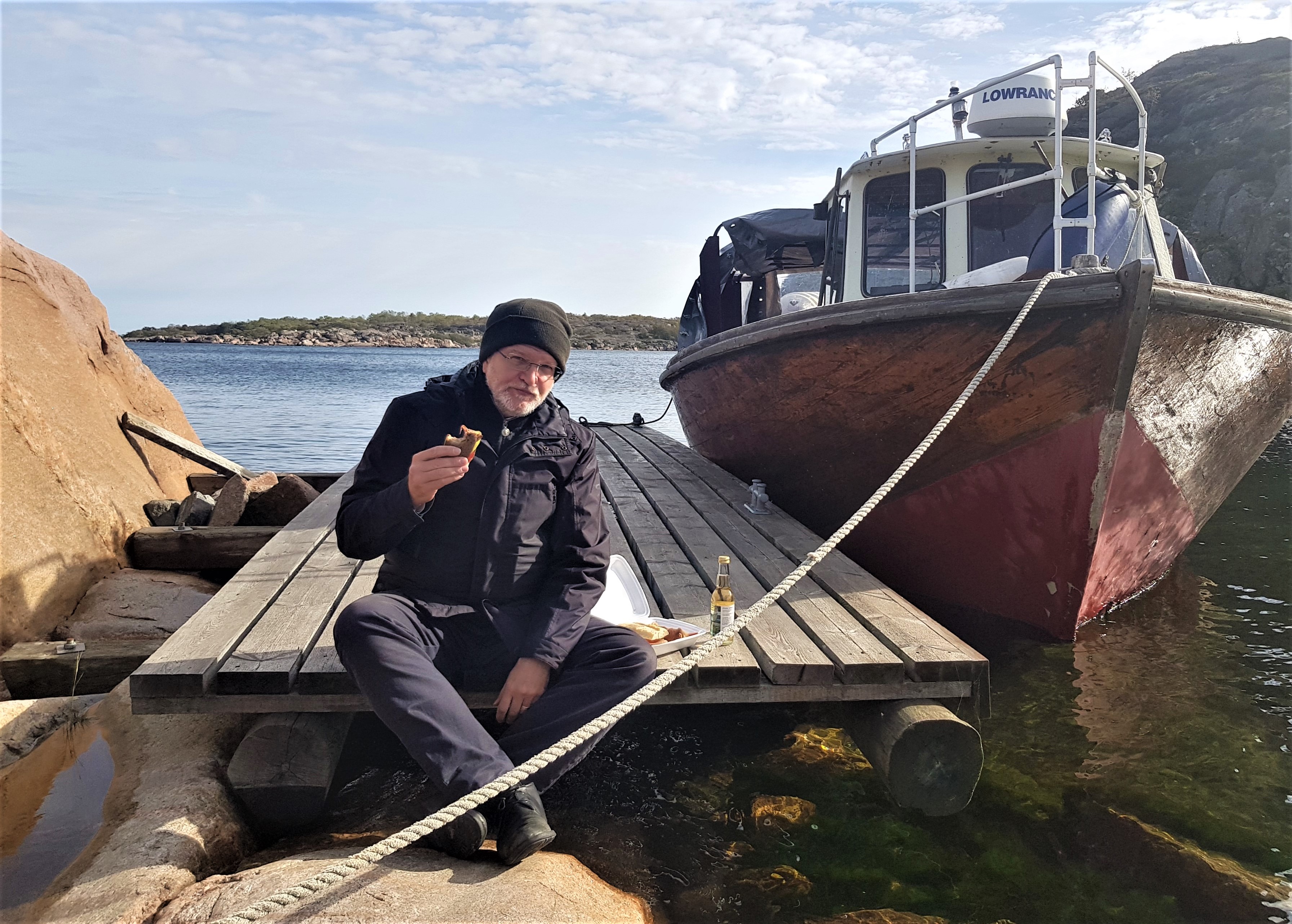 En nöjd man sitter på en bryggkant och skålar i äppelmust.