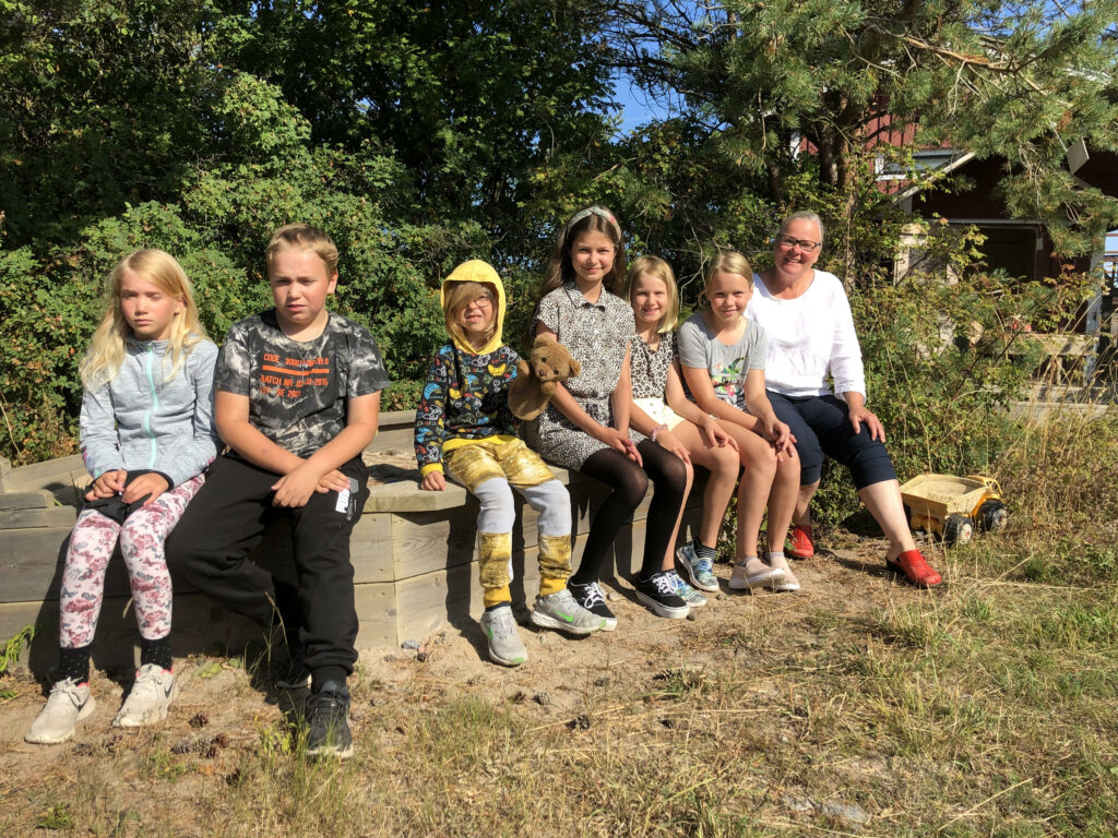 På rad ute i solskenet sitter Isa och Emil Mattsson, Ida och Matilda Alanne, Jadessa Mäkynen, Luca Mellin och läraren Tytti Pesu.