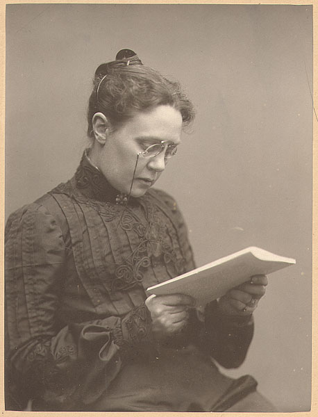 Helena Westermarck (i halvprofil sittande och läsande en bok med glasögon och håret uppslaget i en knut).